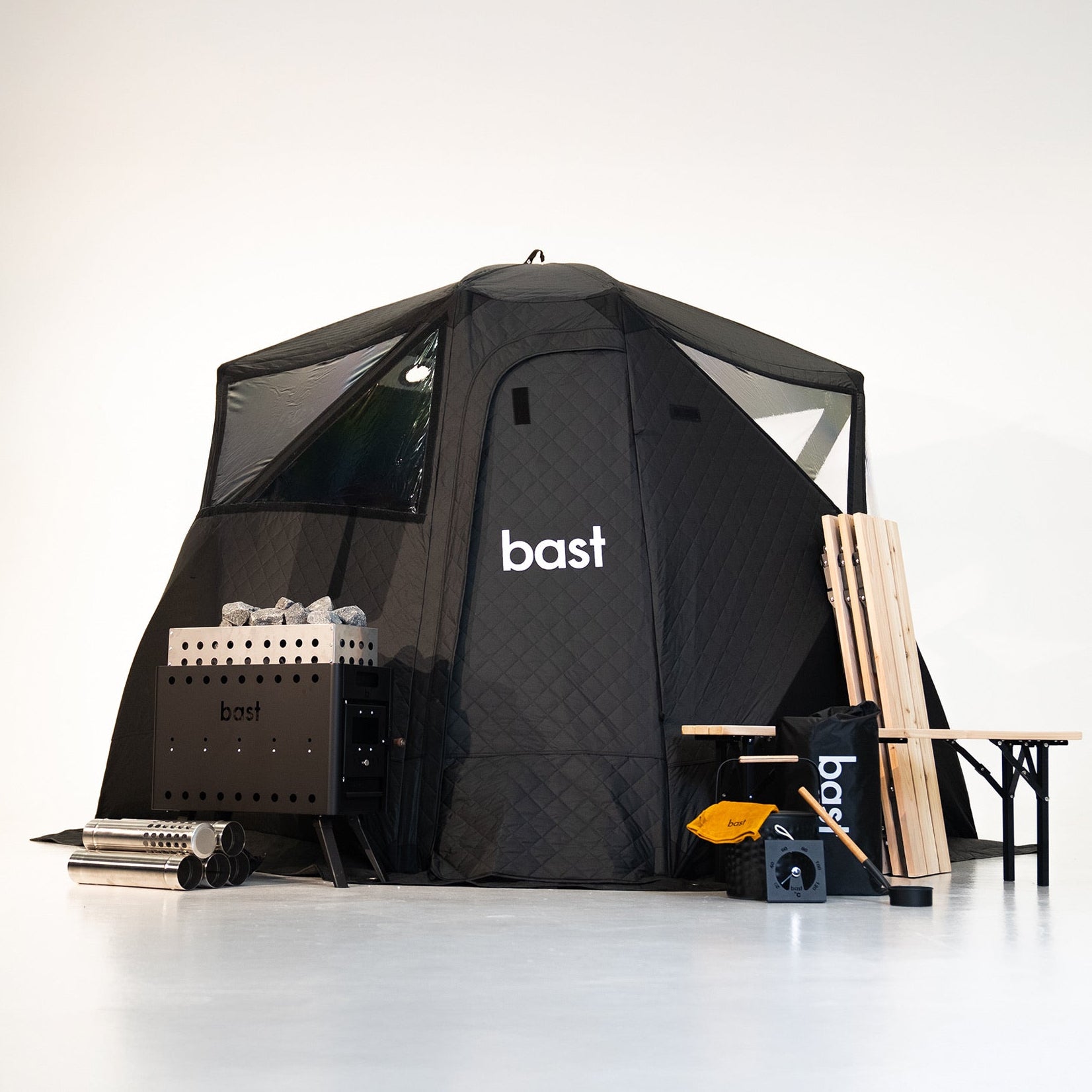 Black outdoor sauna tent with 'bast' branding, surrounded by sauna equipment and accessories on a white background