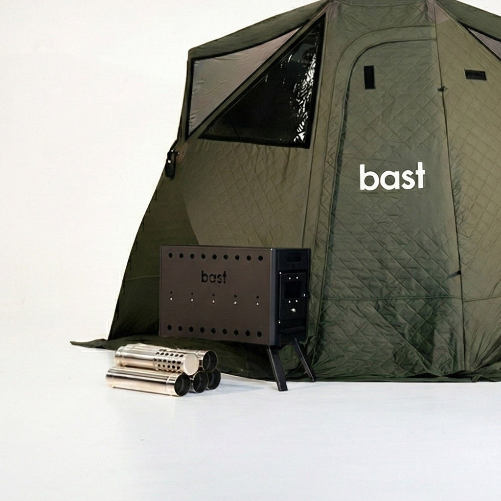 green outdoor sauna tent with 'bast' branding, surrounded by sauna stove and equipment on a white background