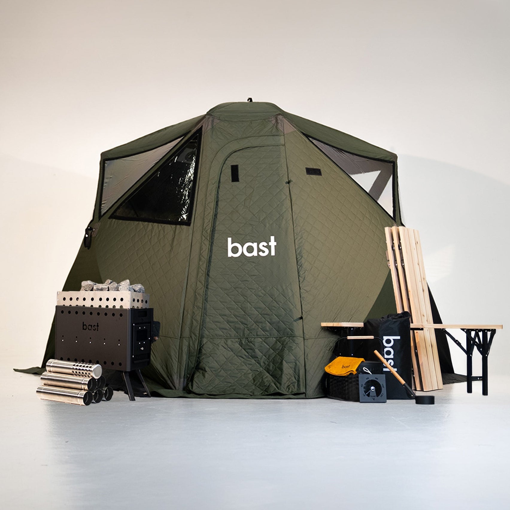 green outdoor sauna tent with 'bast' branding, surrounded by sauna equipment and accessories on a white background