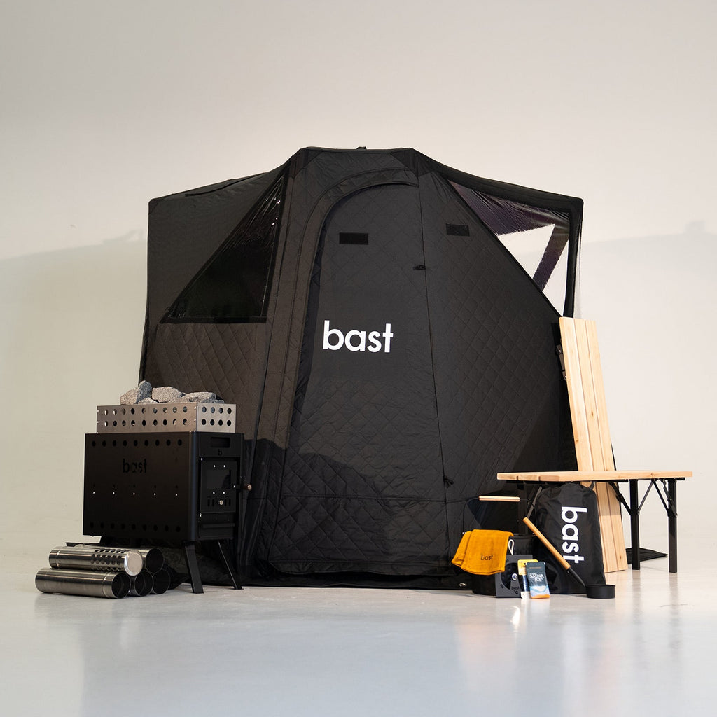Black pop-up sauna tent stove and wooden bench with 'bast' branding on a white background