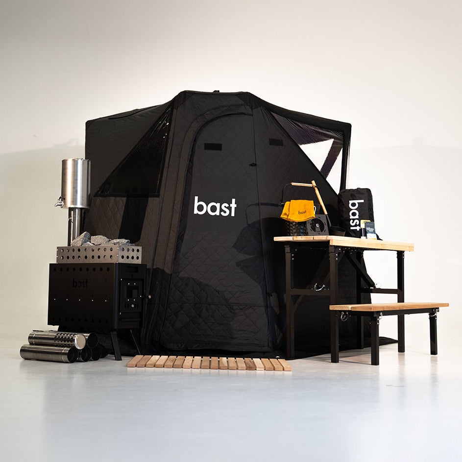 Black 'bast' branded sauna tent with bench and sauna stove with equipment on a white background