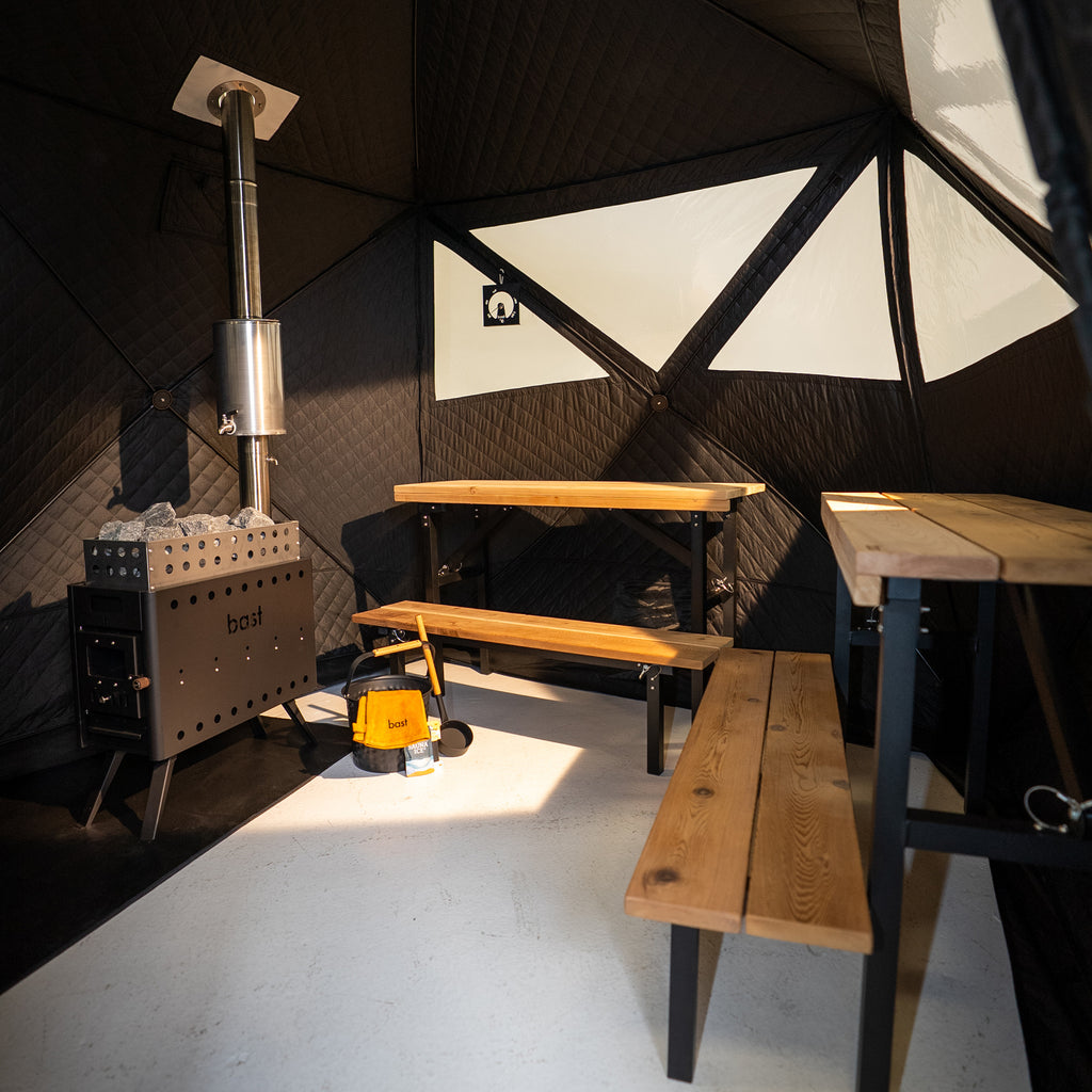 Indoor sauna tent chamber with wooden  benches, stove and equipment against a geometric black and white wall.