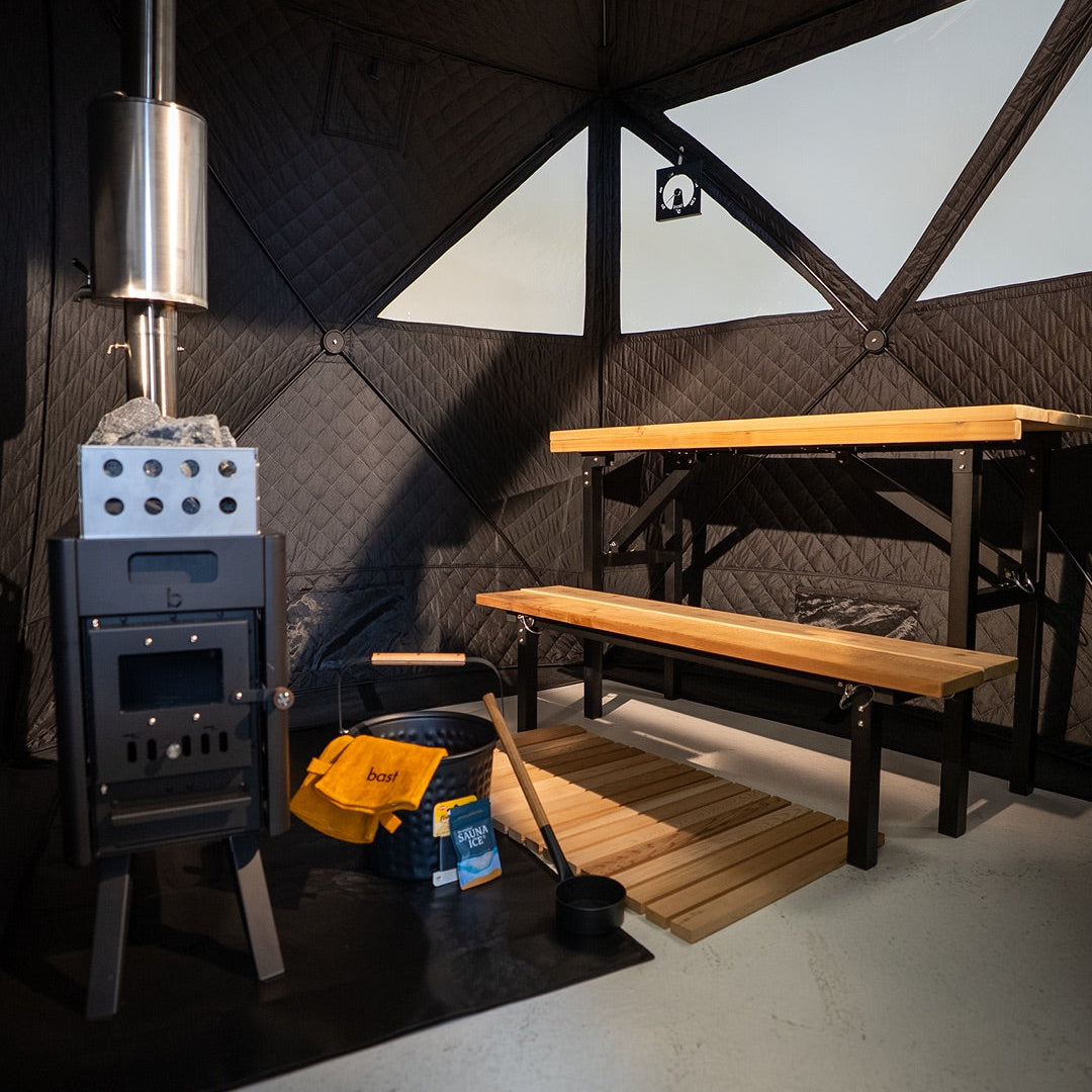 Wood-burning stove in a small room with wooden table and bench.