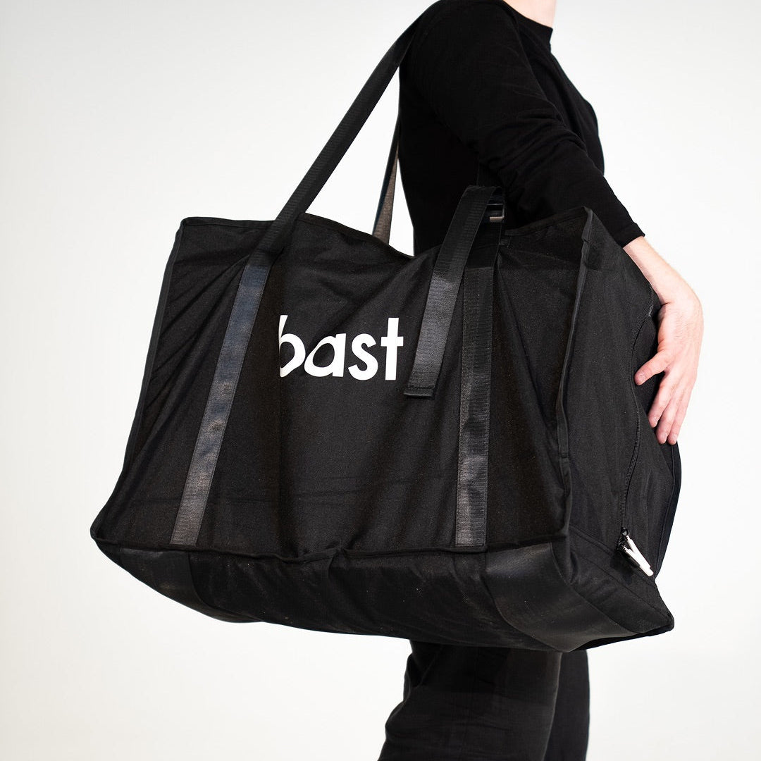 Person holding a black duffel bag with 'bast' branding on a light gray background