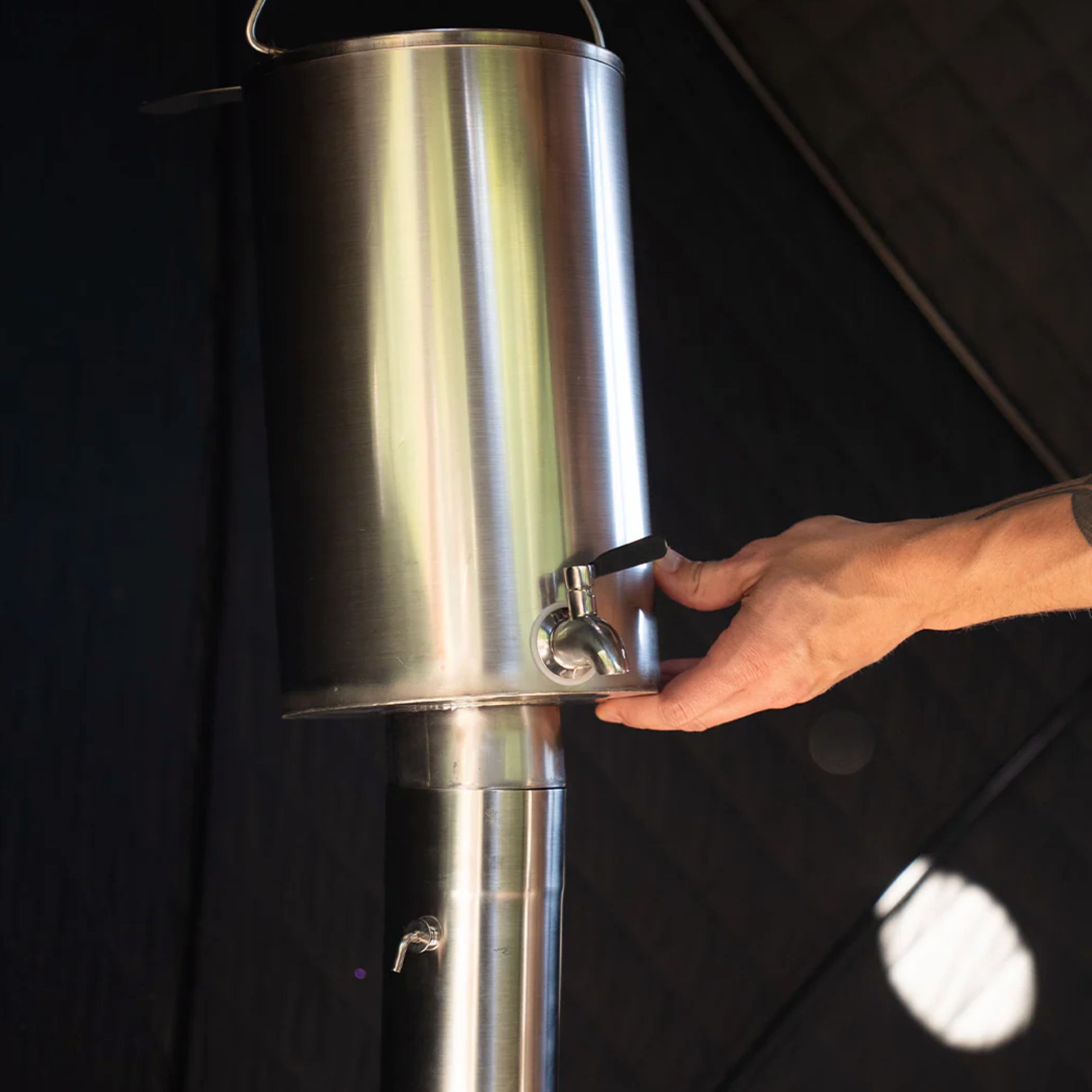 Stainless steel container for heating water with a hand adjusting a valve against a black background