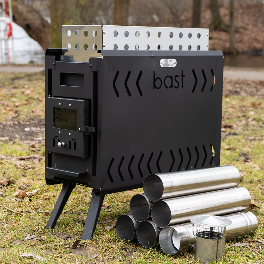 Black stove with 'bast' branding and spare metal parts on a grassy area.