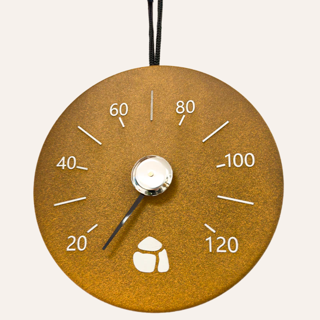 Round gold-colored thermometer with white markings on a light gray background