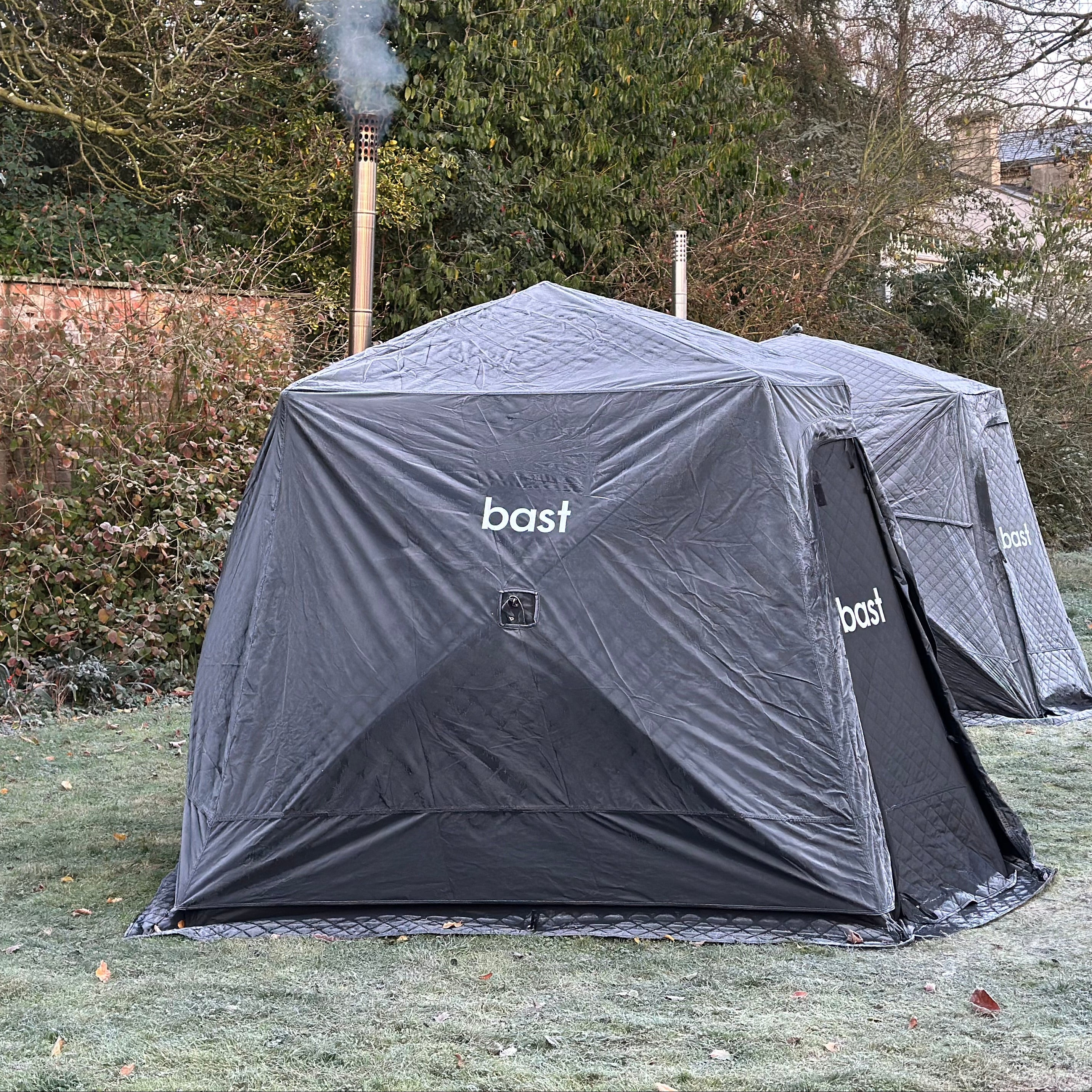 two black sauna tents with 'bast' branding in frosty condition on a grassy area.