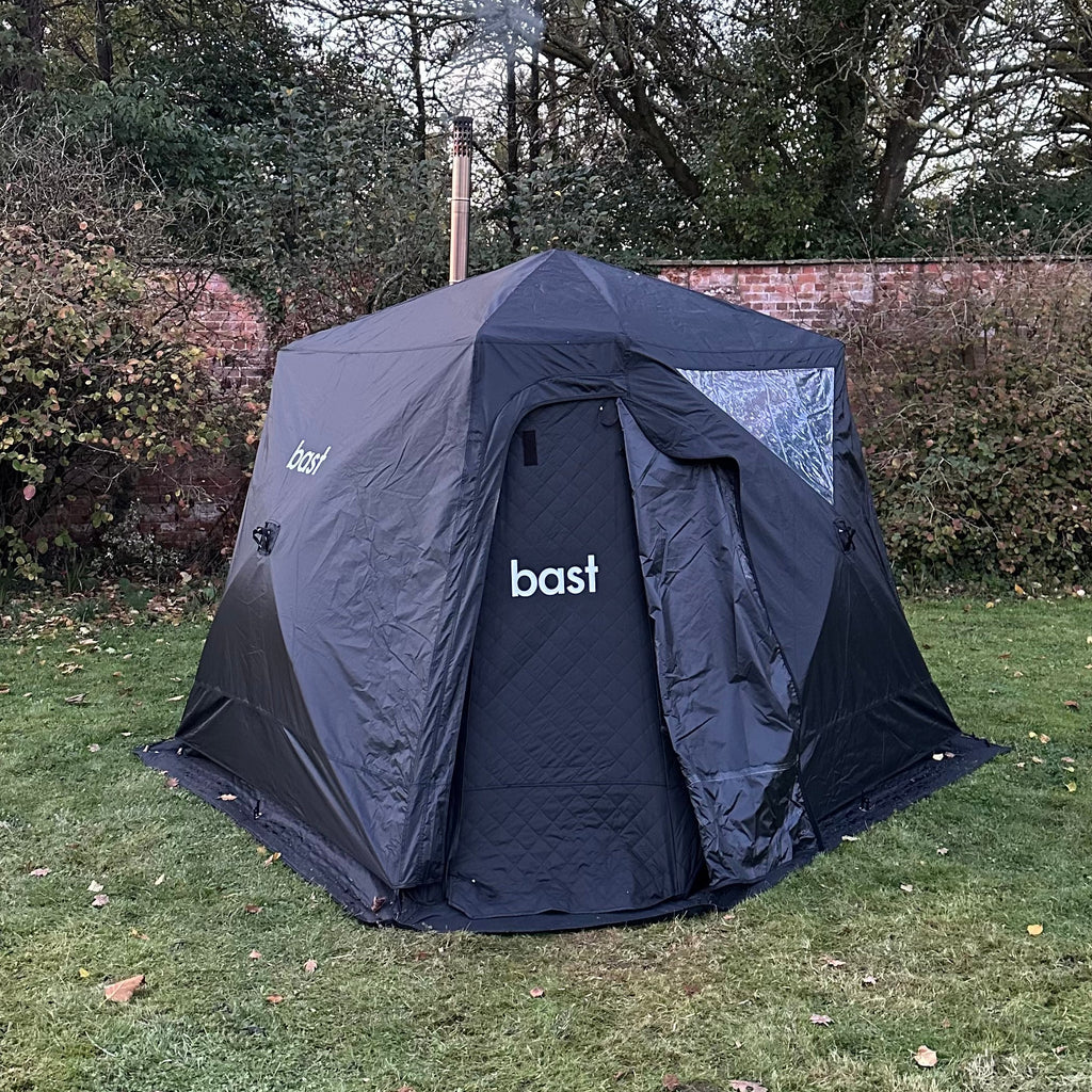 Black sauna tent with 'bast' branding on a grassy area with trees in the background