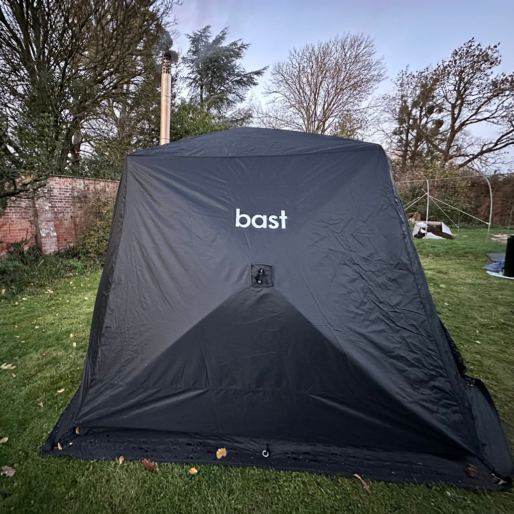 Black sauna tent with 'bast' branding on a grassy outdoor area