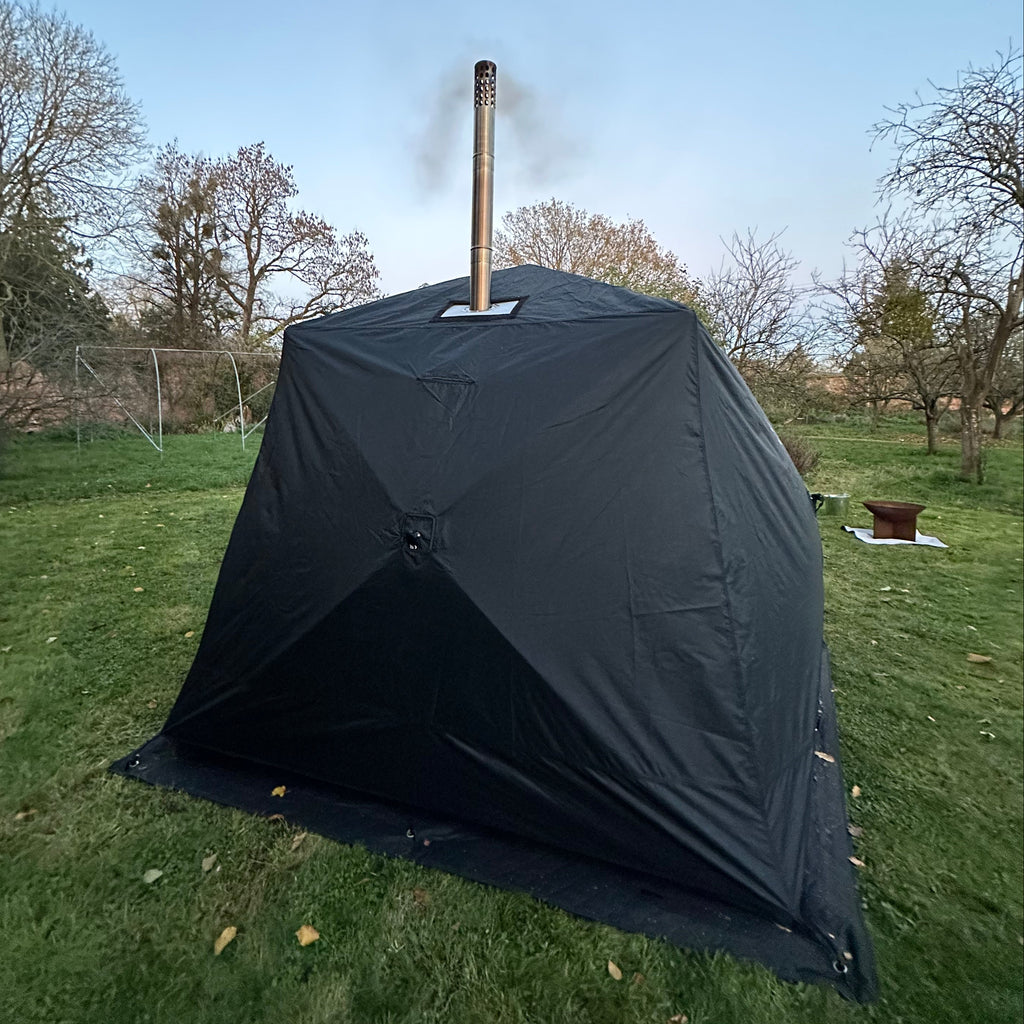 black sauna tent with a 'bast' logo on grass with trees and clear sky in the background