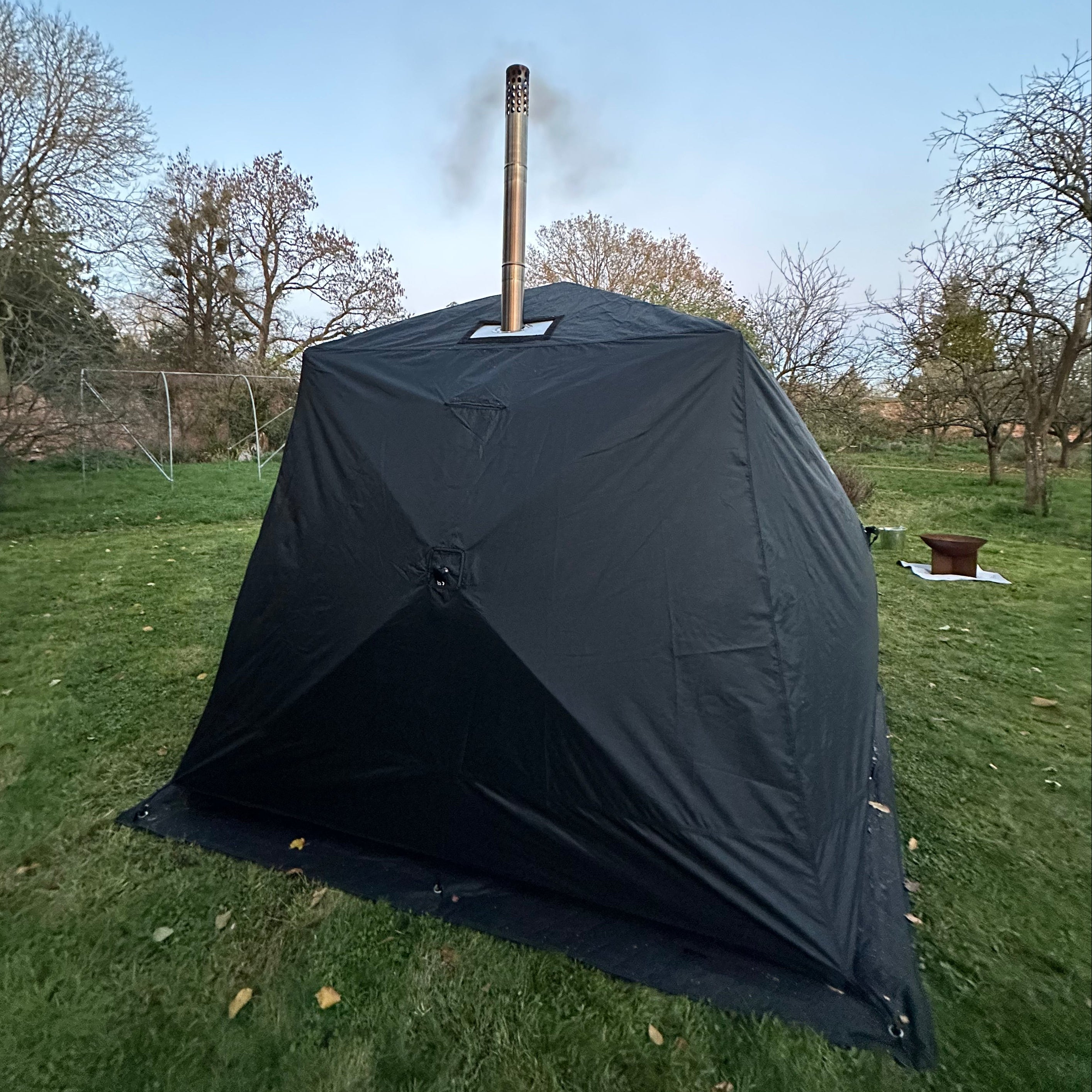 black sauna tent with a 'bast' logo on grass with trees and clear sky in the background