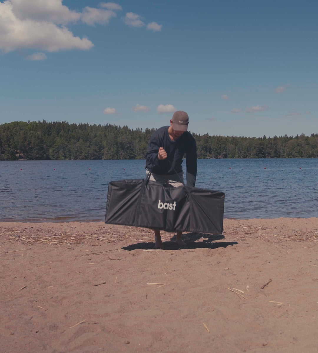 a man assembles a folding wooden bench on beech in a outdoor environment with water and woodland in the background